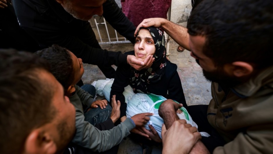 People try to comfort a woman holding the body of her baby girl in the courtyard of the Al-Najjar hospital