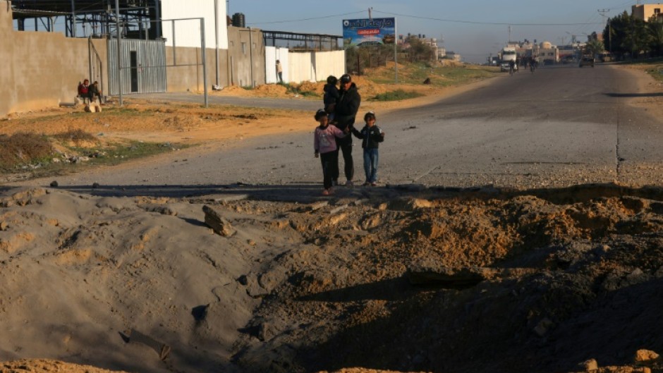 Palestinians fleeing Khan Yunis in the southern Gaza Strip further south toward Rafah stare at a bomb crater in the Salah Al-Din road