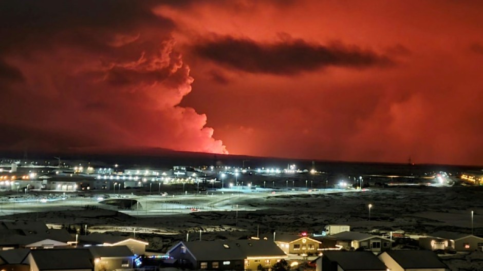 Houses in Iceland's Hafnarfjordur are seen as smoke billows in the distance, the night sky turned orange by lava from an volcanic eruption