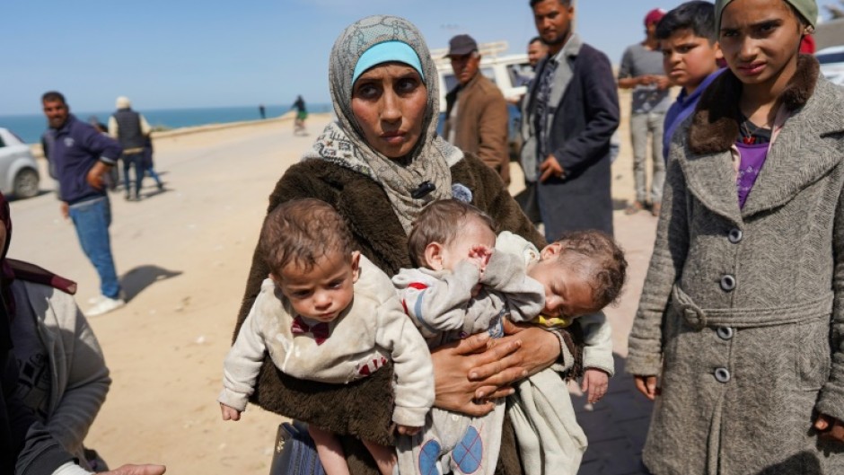 A woman carries three babies in the central part of the Gaza Strip after fleeing the Al-Shifa hospital compound in Gaza City on Thursday