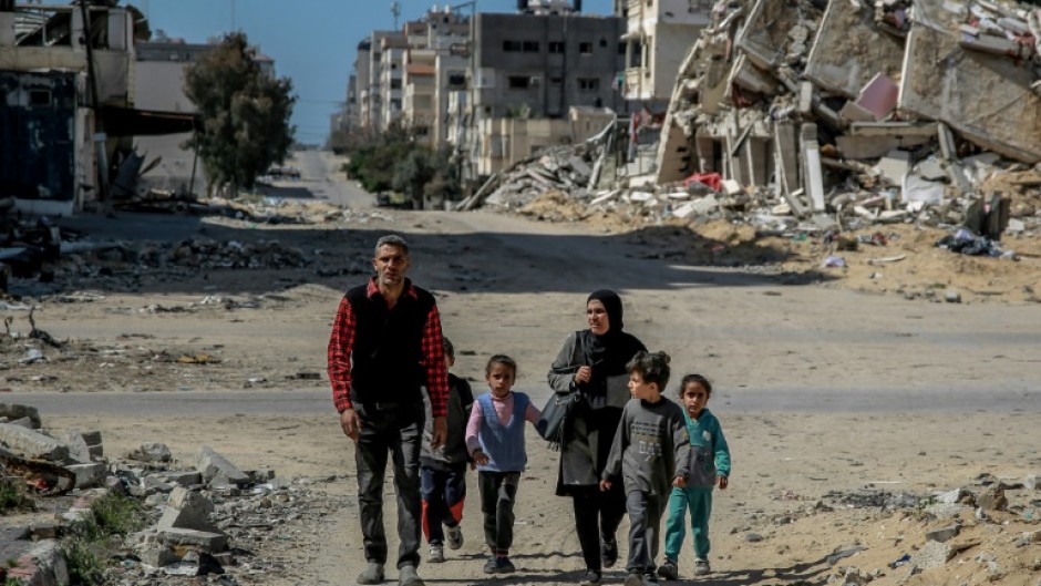 A Palestinian family walk past buildings destroyed in  Gaza City, where the UN has warned that famine is imminent without a major intervention