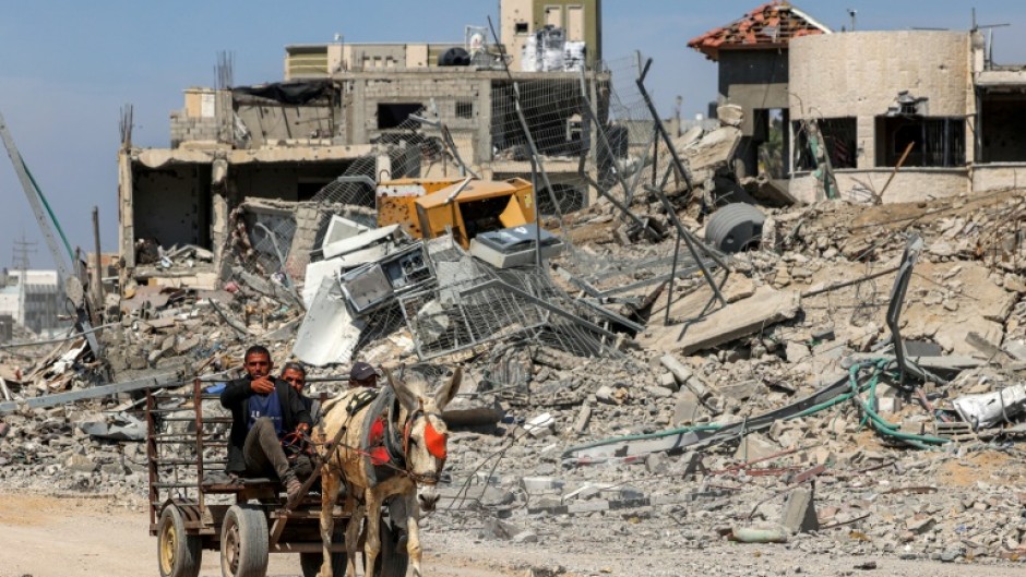 Two men ride a donkey-drawn cart amid the rubble of destroyed buildings in Khan Yunis on April 7, 2024 