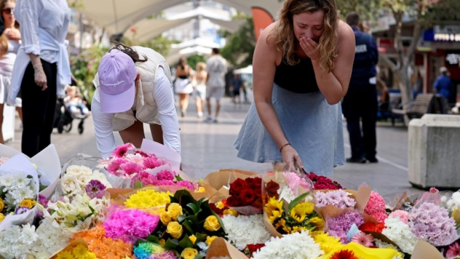 People react as they leave flowers outside the Westfield Bondi Junction shopping mall in Sydney on April 14, 2024