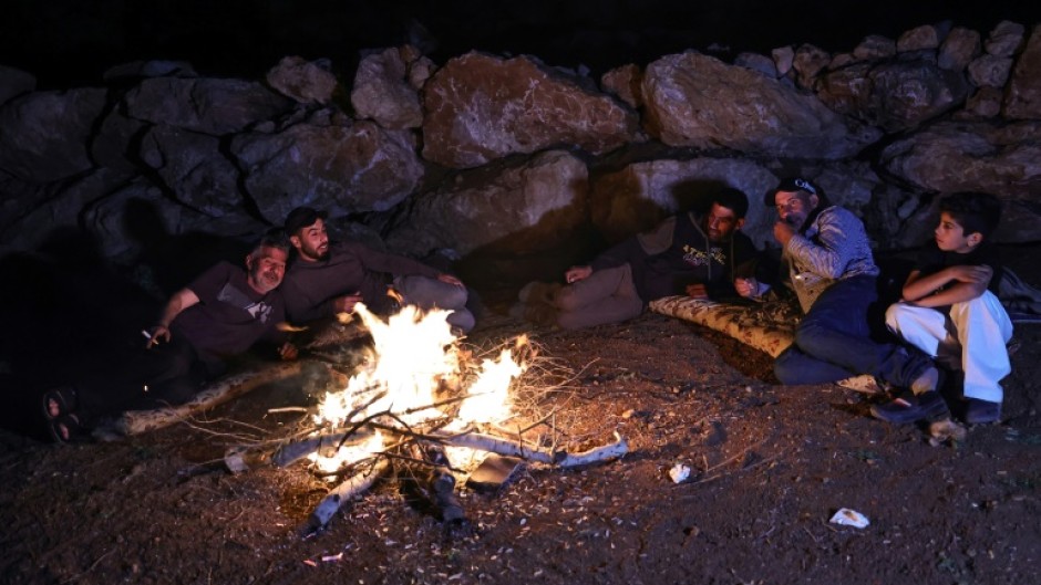 Palestinian men sit around a camp fire as they watch over livestock amid settler attacks in the West Bank