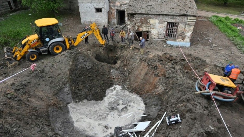 Utility workers operate next to a crater in the courtyard of a hospital in Kharkiv