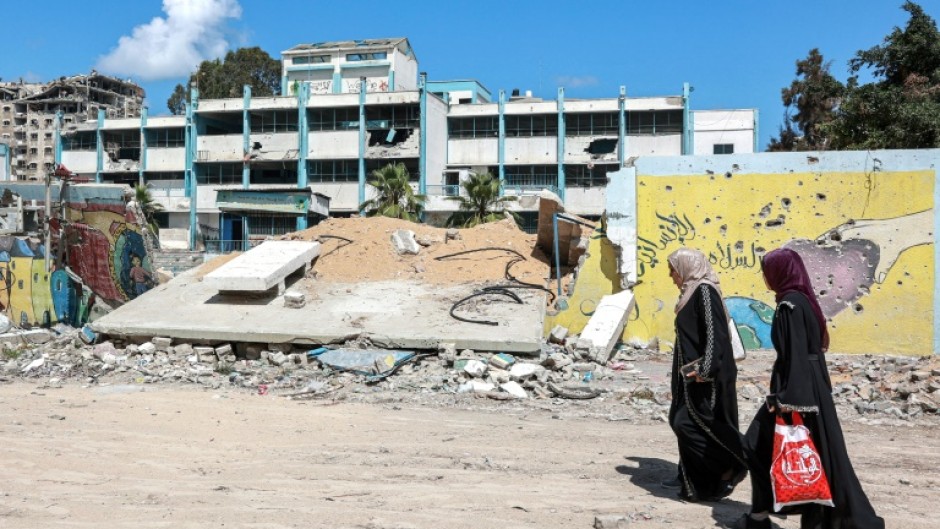 Women walk past the destroyed wall of a school for boys run by the UN agency for Palestinian refugees (UNRWA)