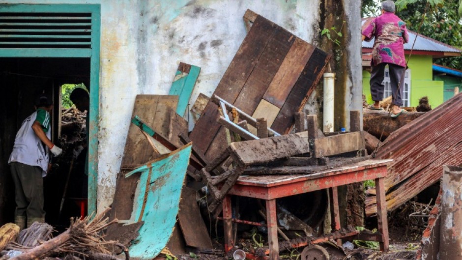 People clean a home that was damaged by mud and logs swept away by flash floods in western Indonesia