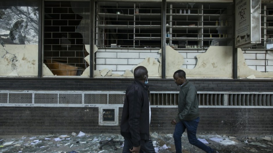 Pedestrians walk past damaged shops vandalised  during the deadly violence which rocked Nairobi over proposed tax hikes