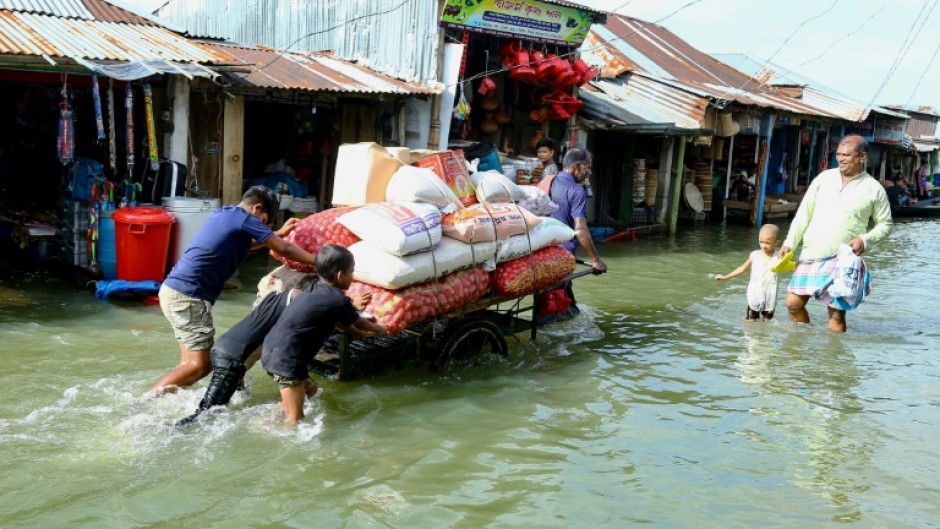 People push a handcart carrying supplies through the flood at Fenchuganj in Sylhet on July 3, 2024