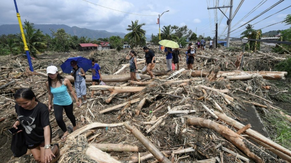 People walk through logs swept away by Tropical Storm Trami in Laurel, Batangas province, south of Manila