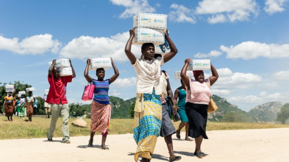 Mothers carry boxes of porridge backed by US aid in the Mutokoarea of Zimbabwe in 2019 as drought worsened hunger
