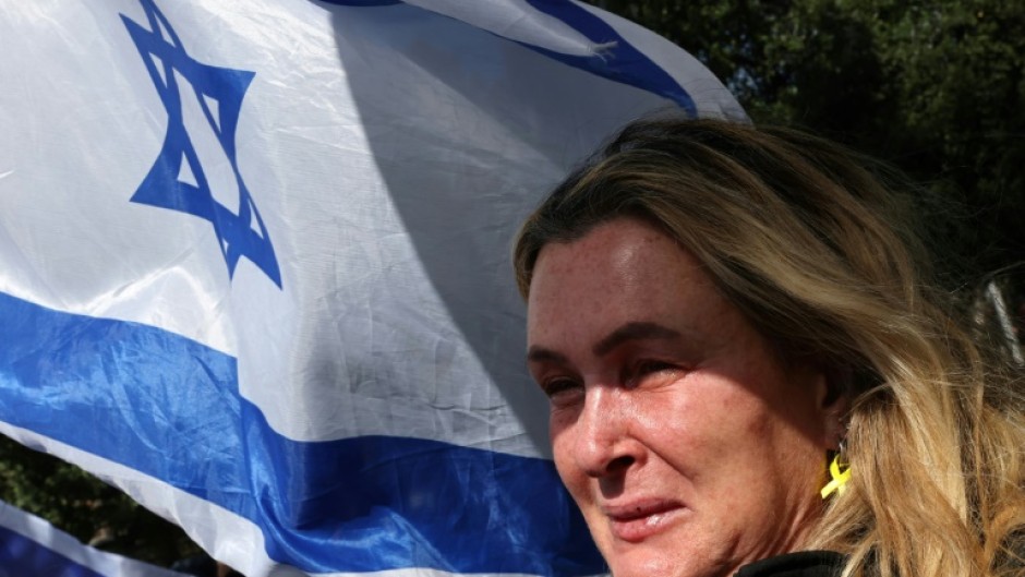 An onlooker holding an Israeli flag cries as a convoy transporting the bodies of dead hostages arrives in Tel Aviv on Thursday