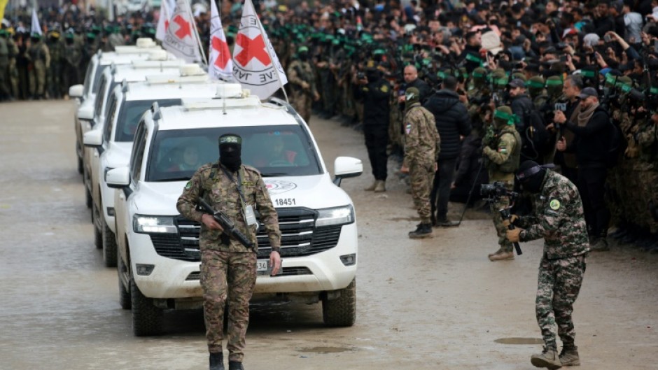 A Palestinian Hamas fighter precedes International Red Cross vehicles as they arrive in the central Gaza Strip to receive three Israeli hostages. Israeli Prime Minister Benjamin Netanyahu has described the described the ceremonies as "humiliating"