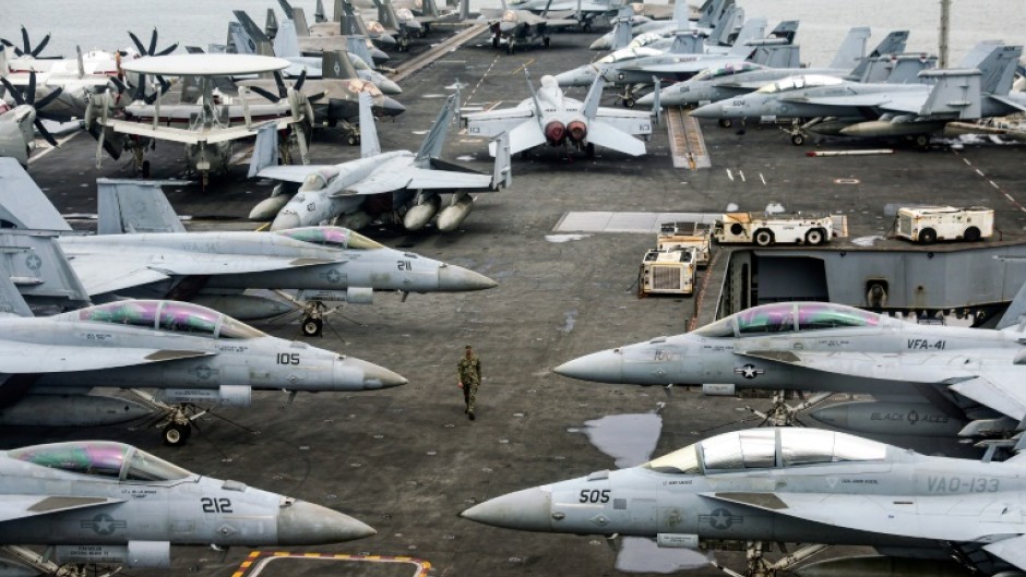 A US Navy officer walks past fighter jets parked on the flight deck of the USS Abraham aircraft carrier