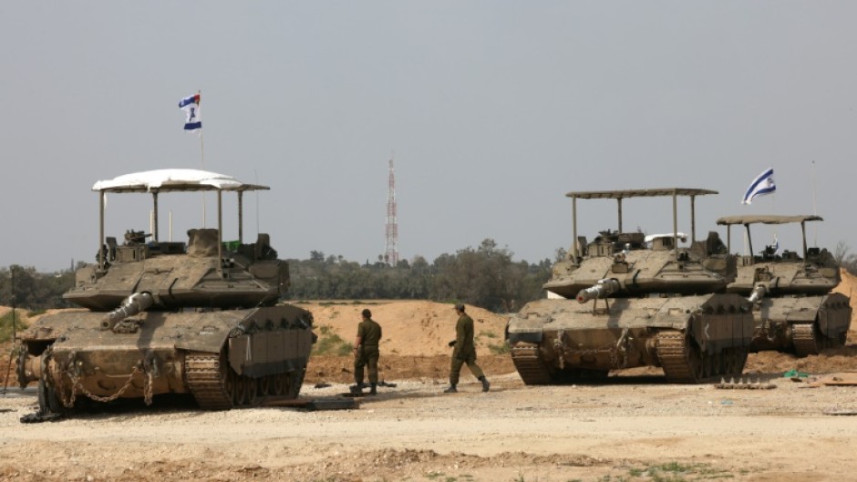 Israeli army soldiers walk past tanks at a position near Israel's southern border with the Gaza Strip