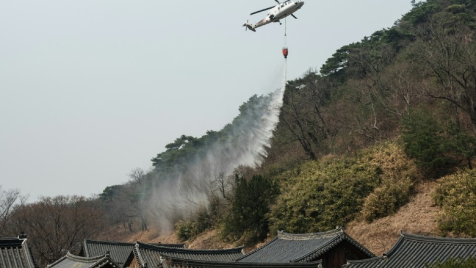 A helicopter drops water as a wildfire advances towards Gounsa Temple in Uiseong