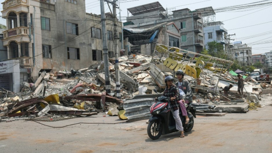 People ride a motorbike past damaged buildings in Mandalay, Myanmar