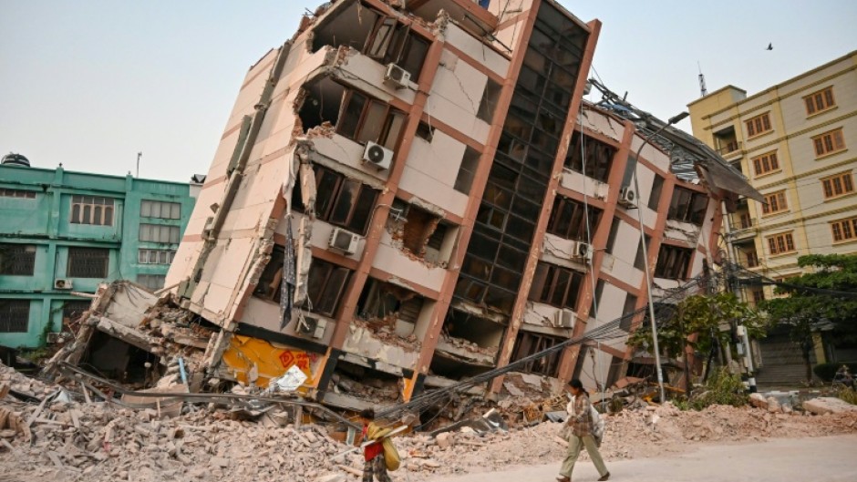 Children walk past a toppled building in Mandalay, five days after the deadly quake