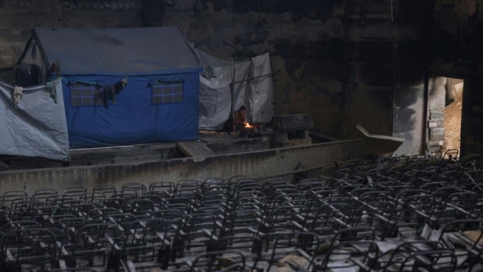 A displaced Palestinian woman cooks a meal on the stage of the auditorium in the heavily damaged Islamic University campus in Gaza City, where Palestinian families have taken refuge