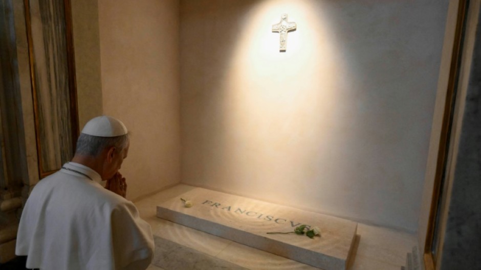 Vatican News published a photo of the white-robed pope kneeling before Francis's simple marble tomb