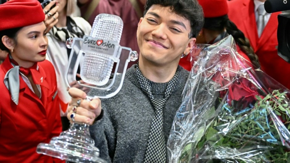 The smiling winner stepped off the plane clutching a bouquet of red roses and his trophy