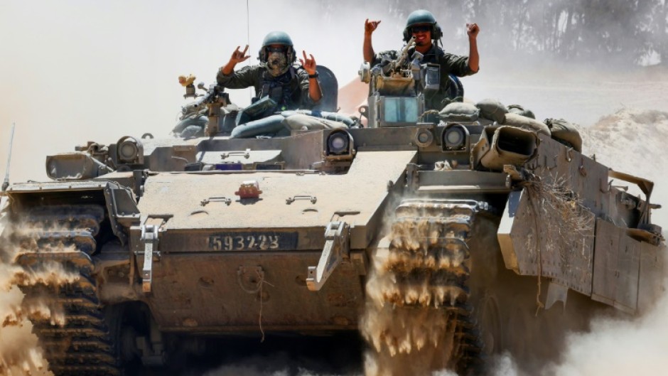 Israeli soldiers gesture atop a military vehicle at Israel's southern border with the Gaza Strip