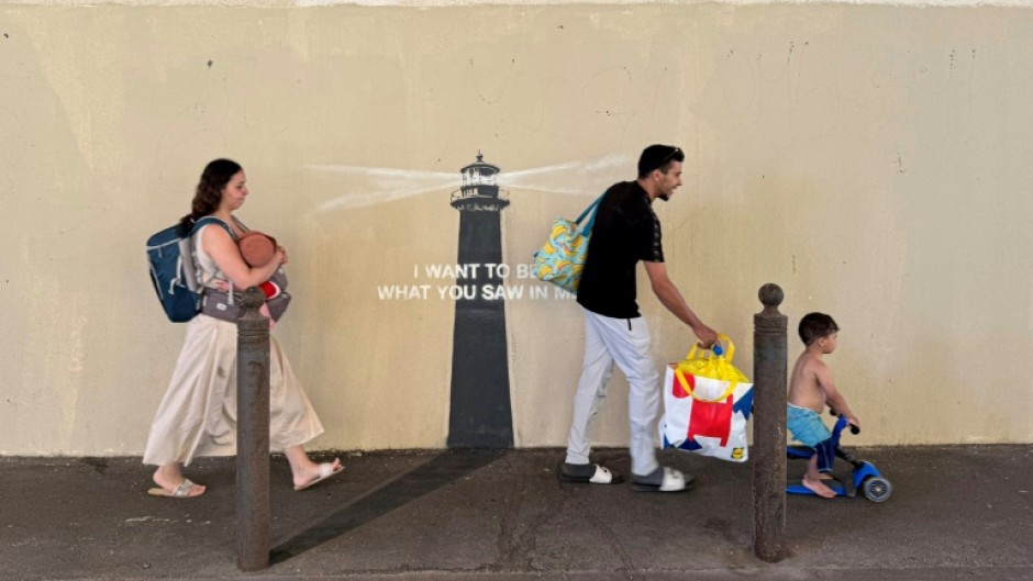 Pedestrians walk past a newly released artwork by street artist Banksy on the facade of a building in Marseille in southern France
