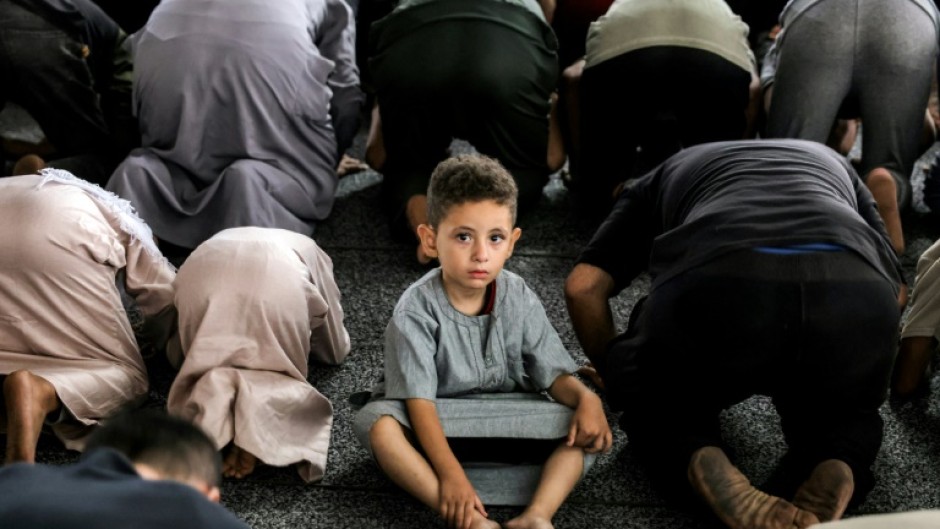 A boy looks on as he sits between Muslim worshippers prostrating as they perform the early morning prayers for Eid al-Adha