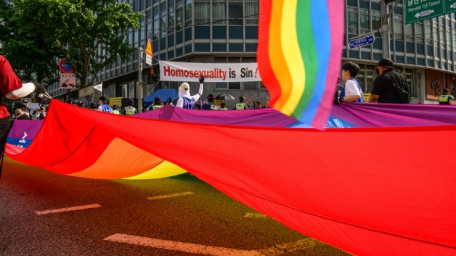 Participants in South Korea's annual Pride parade in Seoul carry a huge flag in support of LGBTQ rights past opponents holding a banner that reads "Homosexuality is sin!"