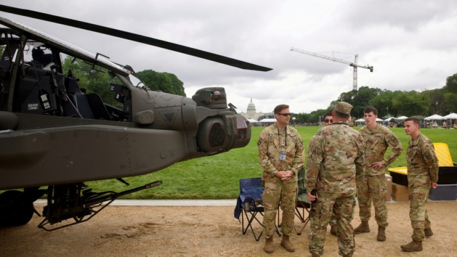 Soldiers gather next to an US Army AH-64 Apache helicopter on display on the National Mall during the Army 250th anniversary celebration
