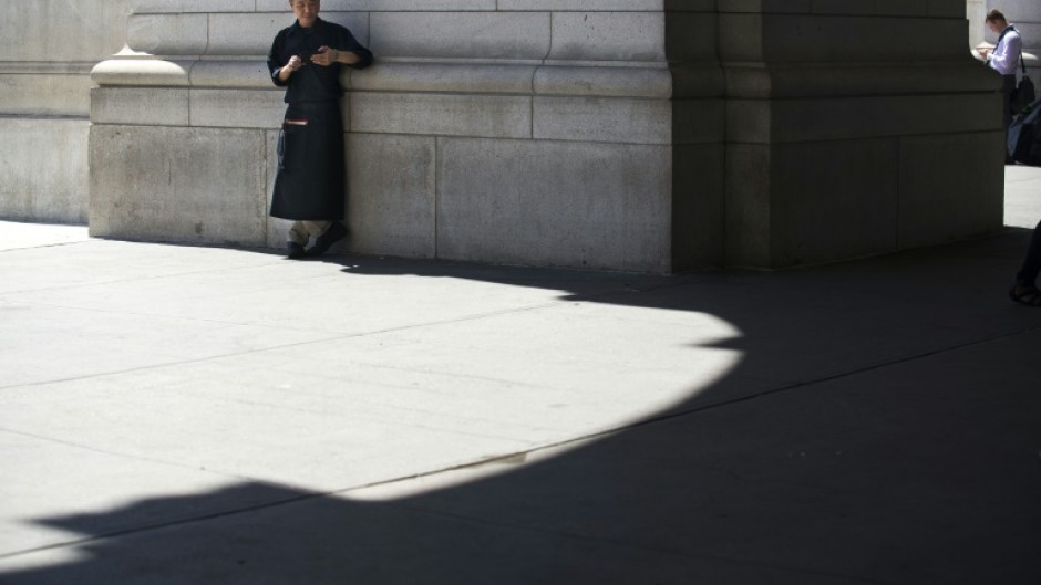 A chef takes a break to check his phone in a sliver of shade outside Union Station on August 12, 2016 in Washington,DC