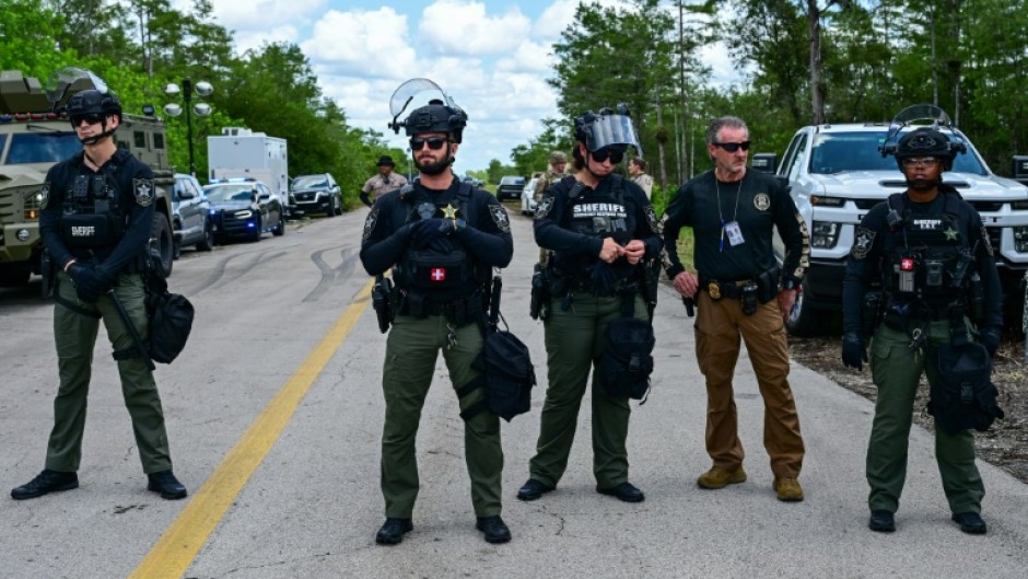 Police officers stand guard as demonstrators protest US President President Donald Trump's visit to "Alligator Alcatraz"