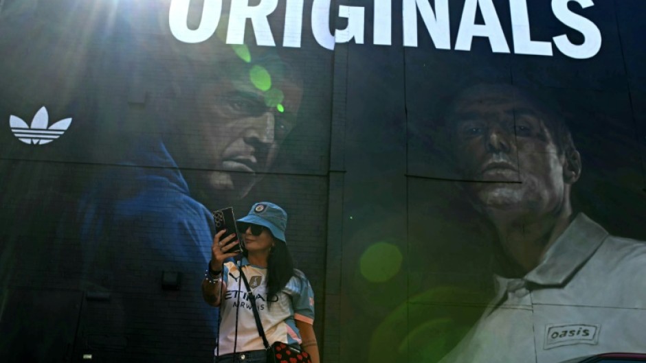 An Oasis fan takes a selfie in front of mural of the band's Gallagher brothers in their Manchester hometown