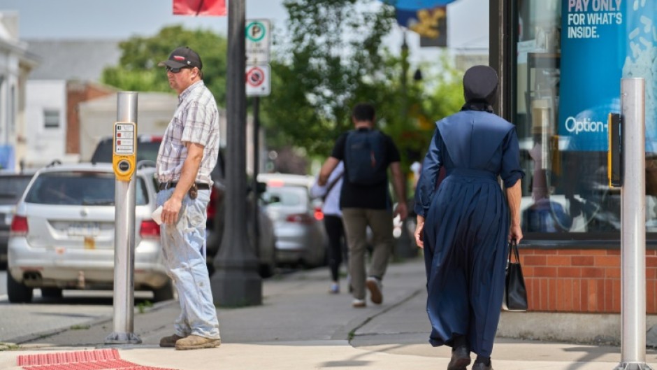 A woman dressed in traditional Mennonite clothing walks through the downtown of Aylmer, Canada in July