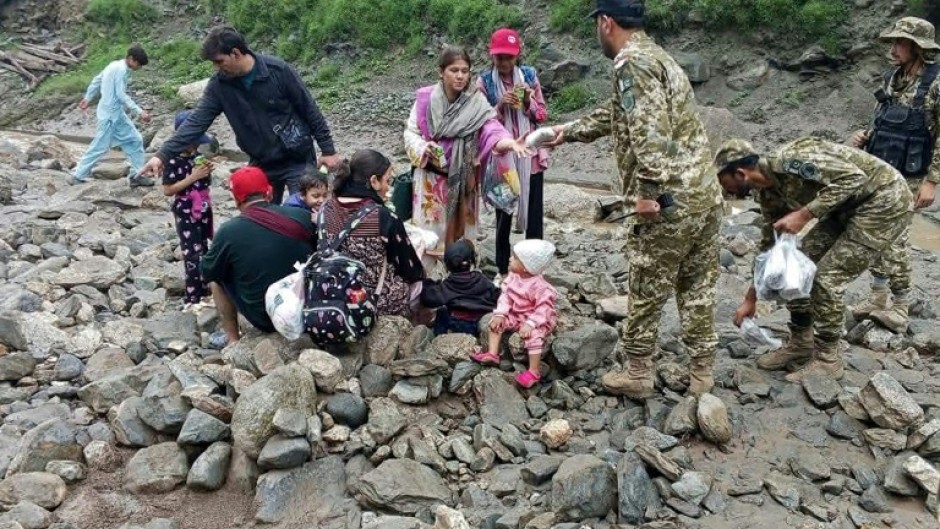 Rescued families holding babies and carrying rucksacks sat on rocks while rescue teams handed them food
