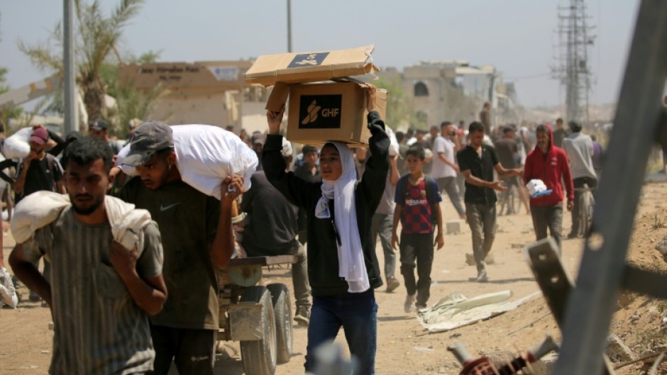 A Palestinian woman carries a food parcel as people return to the Nuseirat refugee camp from a US-backed Gaza Humanitarian Foundation distribution point near the Netsarim corridor in the central Gaza Strip