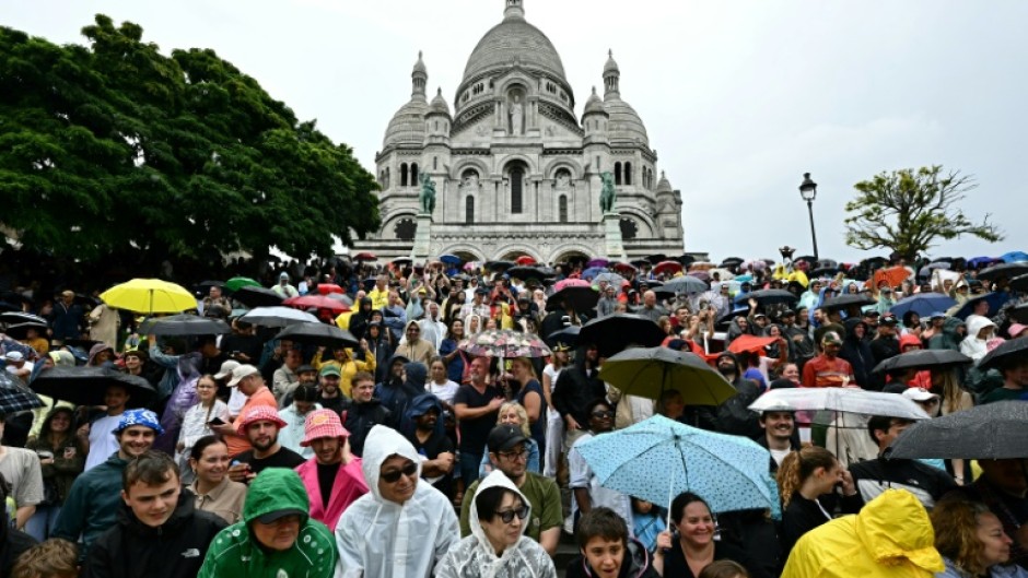 Spectators gather under umbrellas as they await the arrival of the Tour de France riders at the Sacre-Coeur basilica in Montmartre