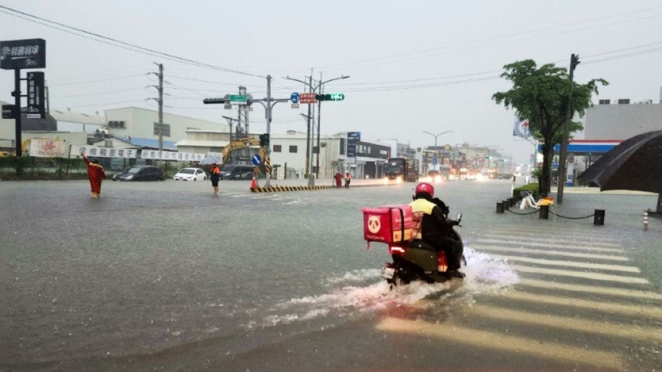 A delivery worker rides a scooter through a flooded intersection in Tainan