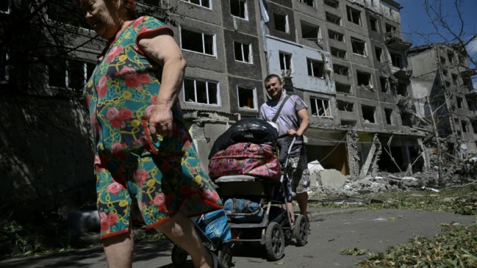 Local residents carry their belongings out of a heavily damaged residential building following a Russian strike in the town of Bilozerske, Donetsk region on August 12, 2025