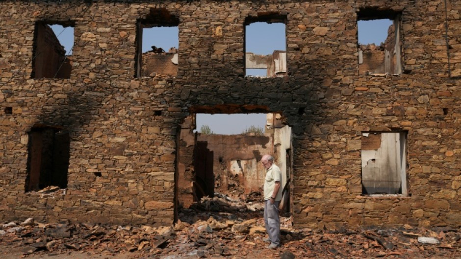 A man stands in front of a ruined burnt house after a wildfire in the village of Castrocalbon, northwestern Spain