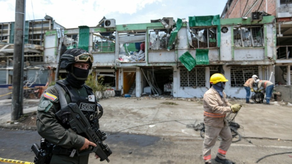 A security member stands guard as cleaners clear debris from the site of a bomb explosion in Cali, Colombia