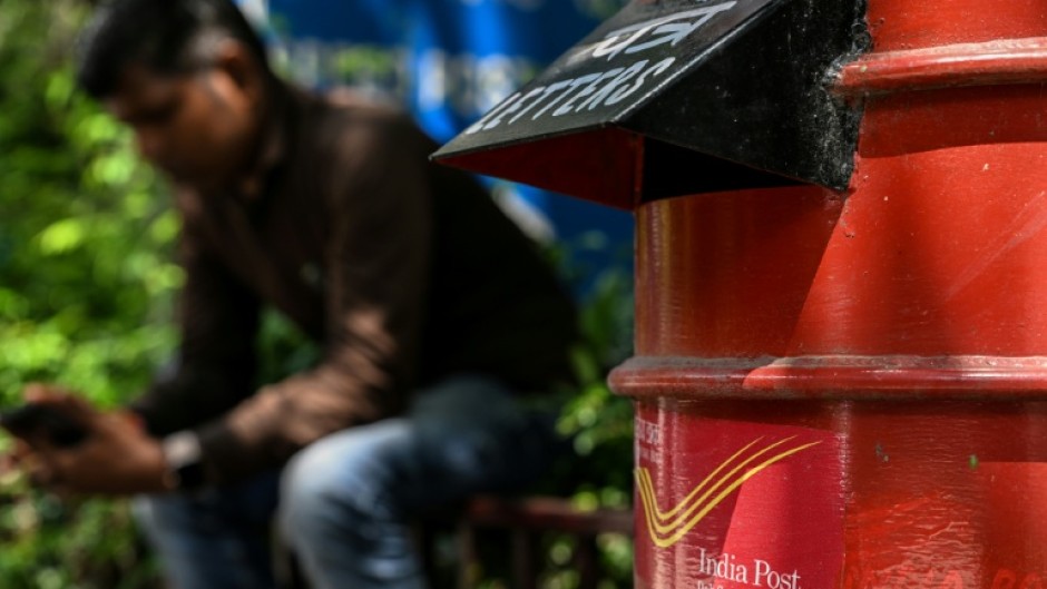 A man uses his mobile phone while sitting next to an India Post box outside its office in New Delhi