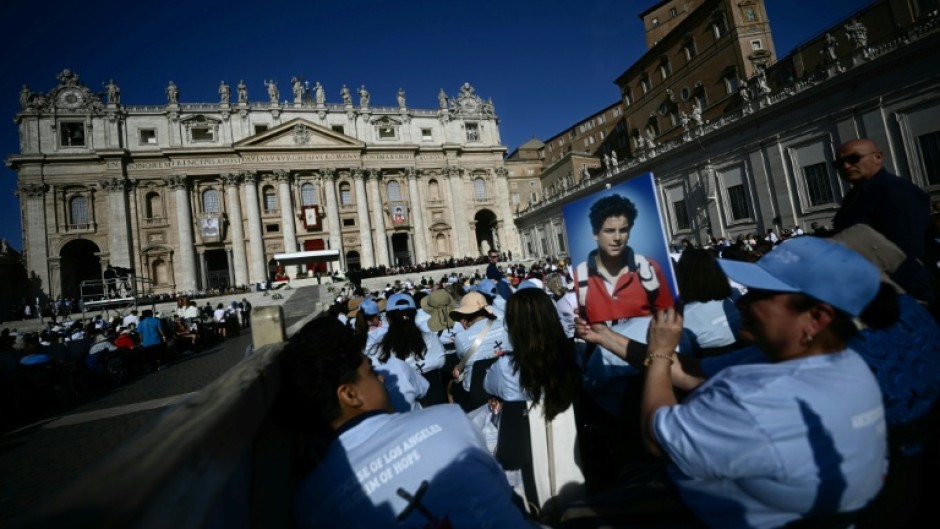 A faithful holds a portrait of late teenager Carlo Acutis in front of Saint Peter's