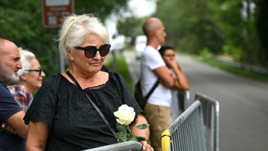 A woman holds a white rose as she waits for the hearse carrying the body of Giorgio Armani