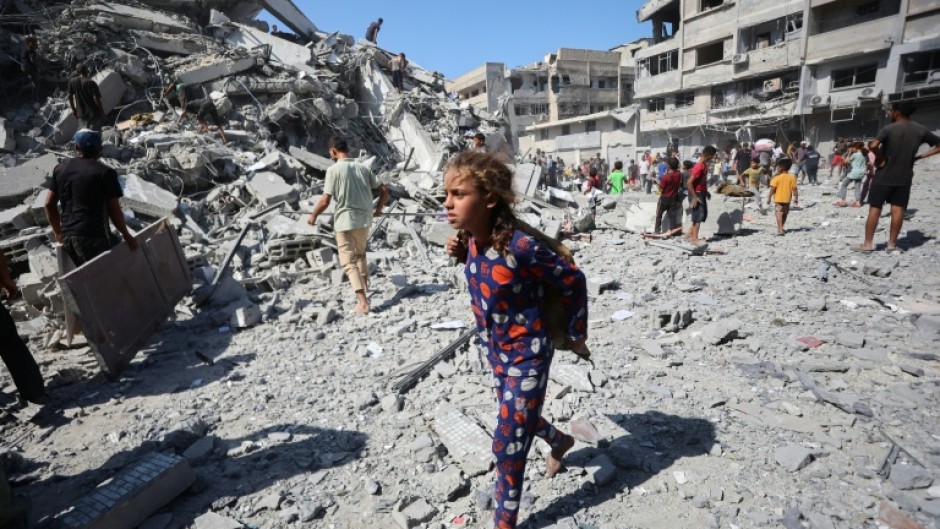 Displaced Palestinians salvage items from the rubble of the Al-Ghafari tower after it was destroyed in Israeli strikes in Gaza City