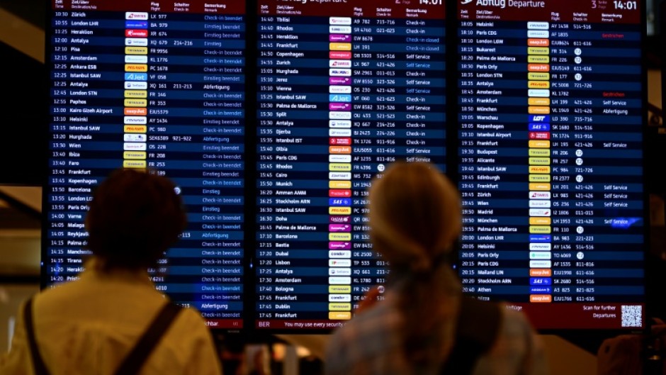 Passengers check a digital display showing flights at Berlin Brandenburg BER airport