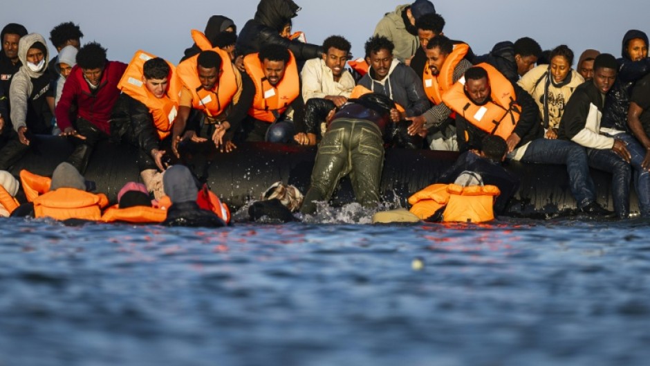 Migrants sitting in a smugglers' boat help others to climb on board in an attempt to cross the English Channel from northern France at the weekend