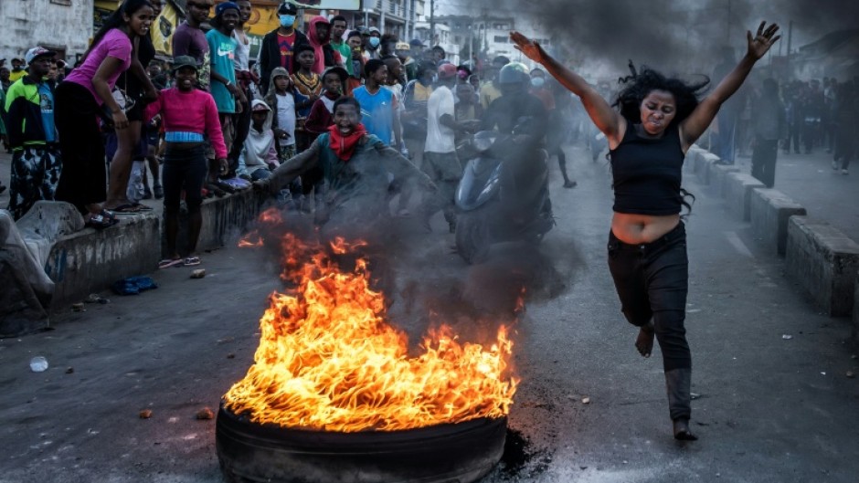 A protester runs past a burning tire used as a barricade during clashes with Madagascar security forces on October 9, 2025
