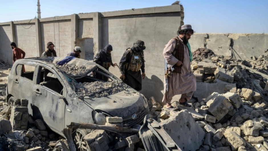 Taliban security personnel walk past a damaged car in the Spin Boldak district of Kandahar province on October 16, 2025, a day after the cross-border clashes between Afghanistan and Pakistan