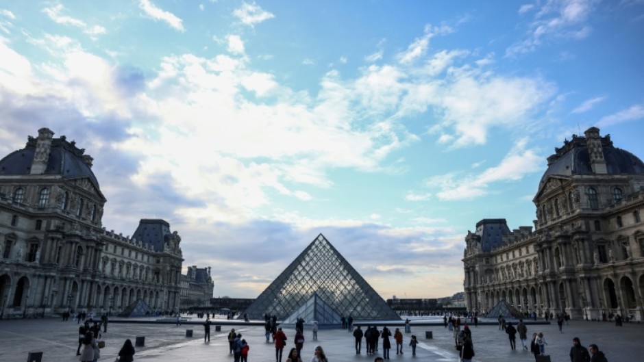 Tourists stroll near the Louvre Pyramid, designed by Chinese-US architect Ieoh Ming Pei, at the entrance to the world-renowned Paris museum, which said it was shutting its doors after a break-in